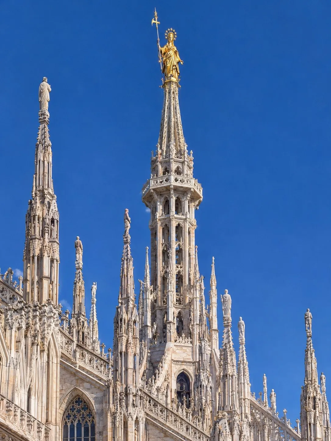 La Madonnina dorée sur la flèche principale du Duomo, vue depuis la terrasse la plus haute sur un ciel bleu